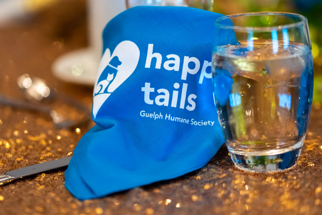 Blue Happy Tails Guelph Humane Society gift bag beside a glass of water on a gala table