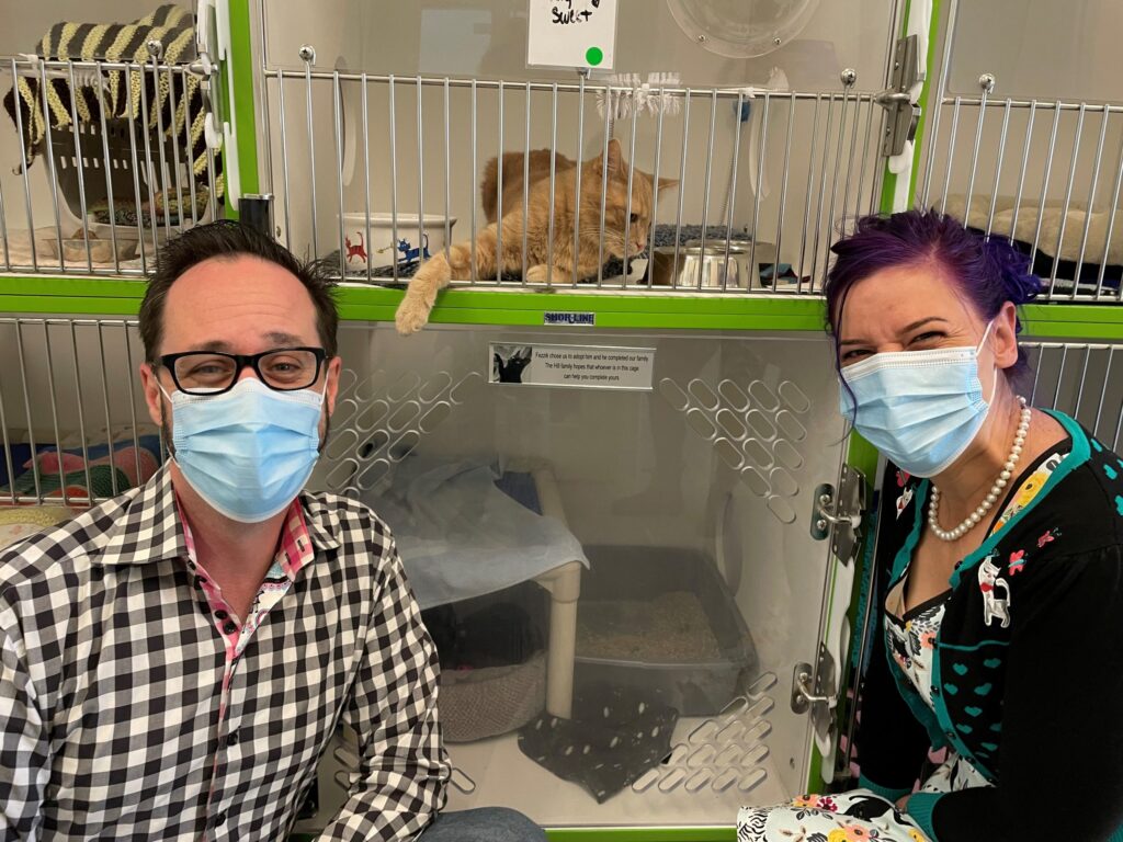 Chris and Melissa, wearing face masks, beside a row of cat kennels