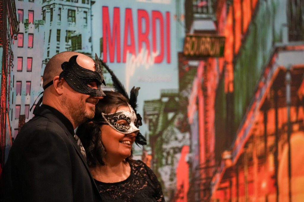 Two guests in masquerade masks posing in front of a Mardi Gras backdrop at the Happy Tails Gala