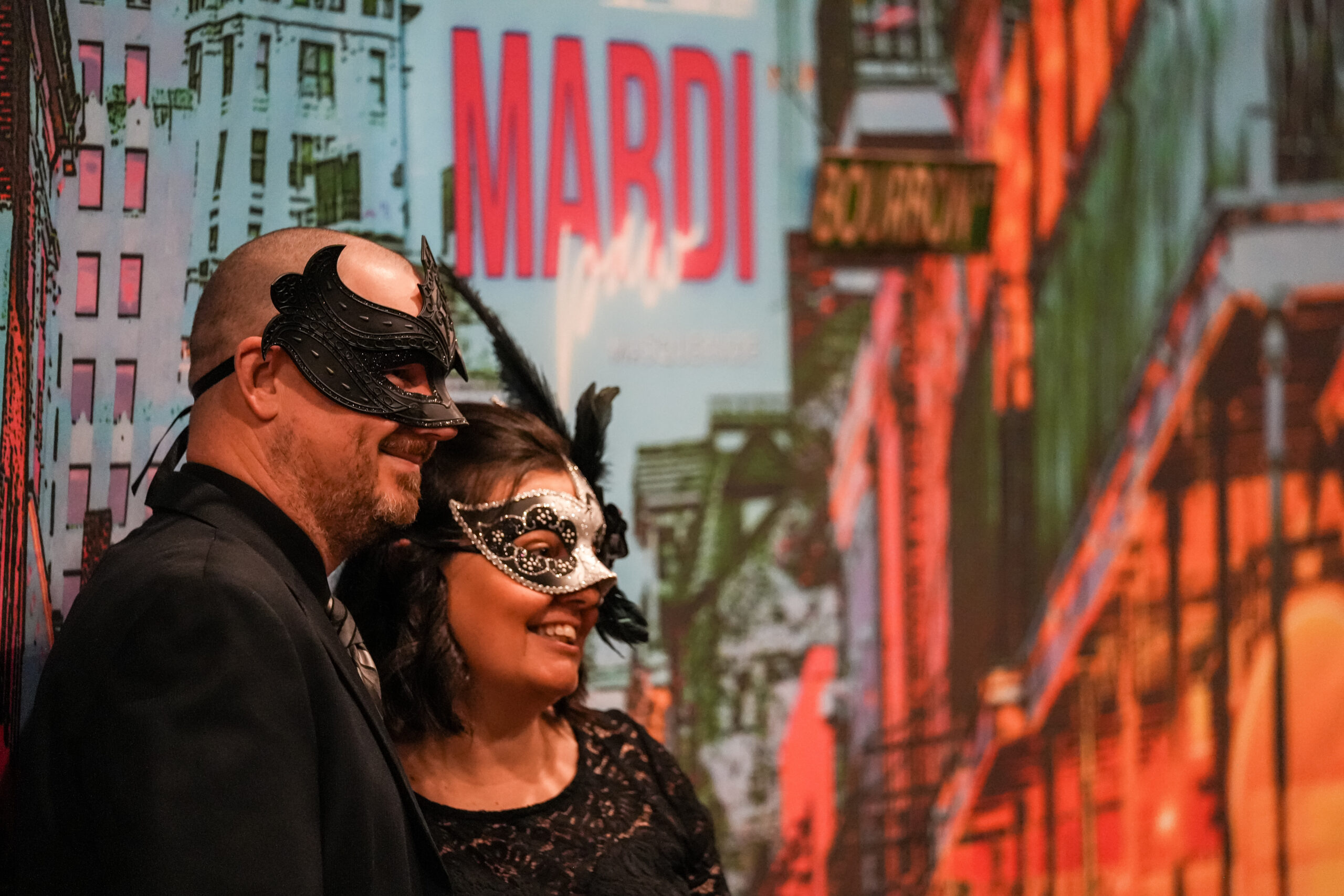 Two guests in masquerade masks posing in front of a Mardi Gras backdrop at the Happy Tails Gala