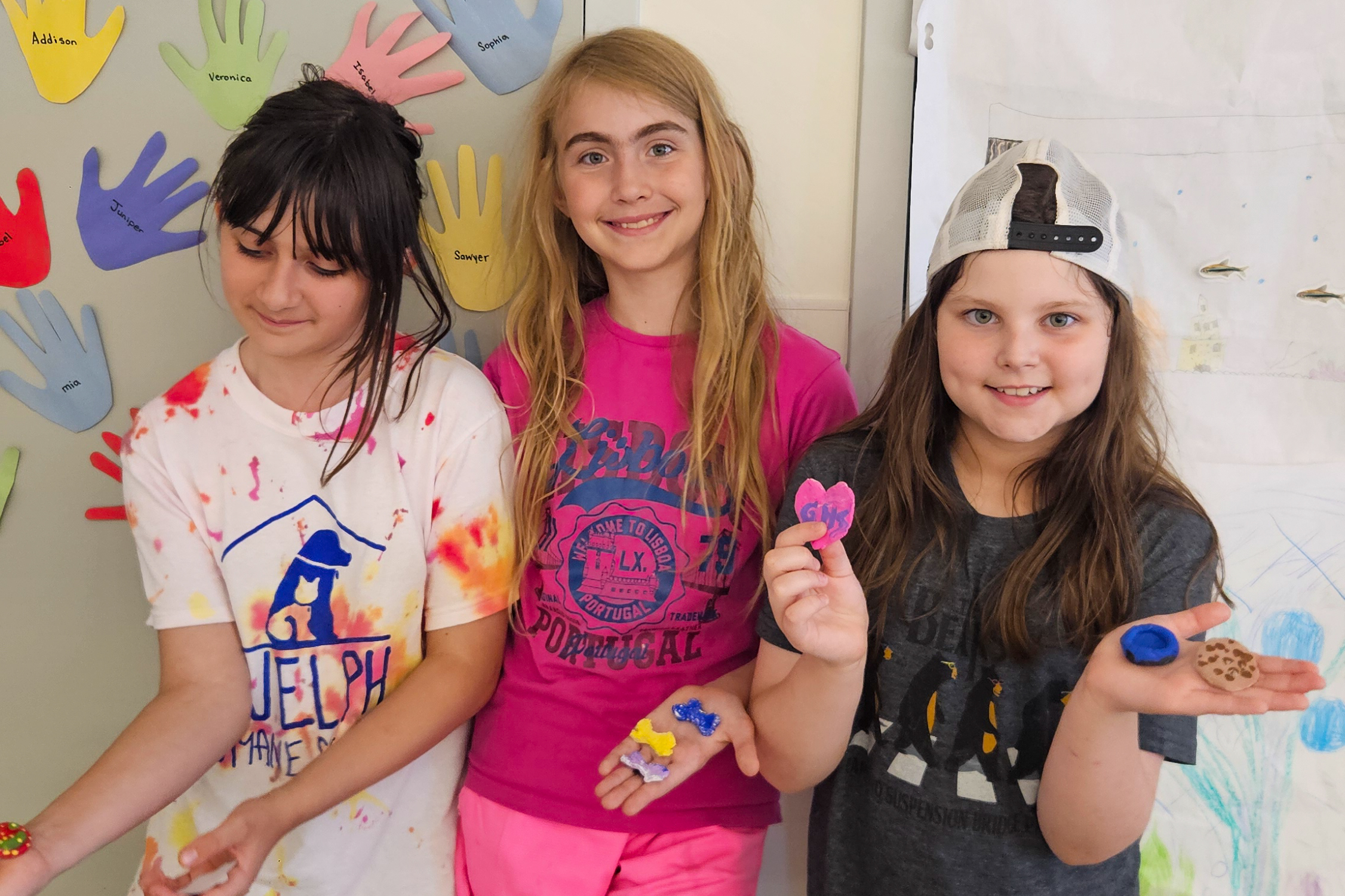 Three smiling girls showing small crafts they made at summer camp